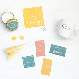 A beautifully arranged gift box designed for special occasions, featuring a vibrant greeting card with the empowering message "She Was Made of Sunlight," a zesty Ray of Sunshine Lemondrops, a calming soy candle, a playful and chic coffee mug, and a set of mini inspirational quote cards.  Perfect for celebrating and uplifting your best gal or sending encouragement to someone special, reminding her of her amazing qualities and how much she's loved.